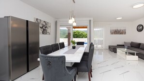 Una cocina moderna con una isla grande, un comedor con una mesa larga y una sala de estar con sofá y mesa de centro.