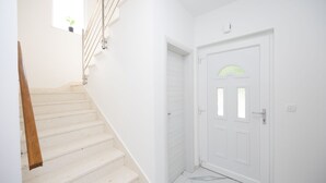 Una escalera blanca que lleva a una puerta con un pequeño ventanal y un interruptor de luz en la pared.