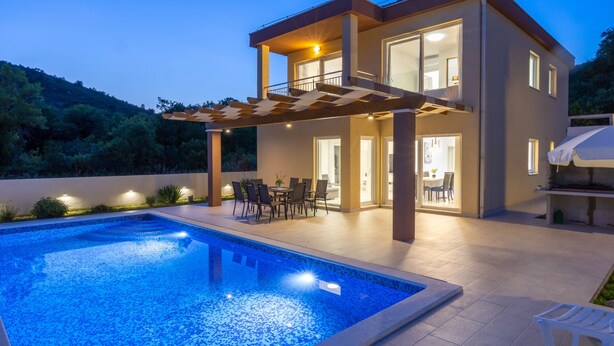 Una casa moderna de dos pisos con piscina, mobiliario exterior y una pérgola.
