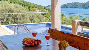 Ein Tisch am Pool mit Früchten und Getränken, Blick auf einen See und eine gebirgige Landschaft.