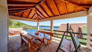 Ein überdachter Außenbereich mit Pool, Holzmöbeln und Meerblick.