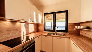 Eine moderne Küche mit Holzarbeitsplatten, einem Backofen, einer Spüle und einem Fenster mit Blick auf das Meer.