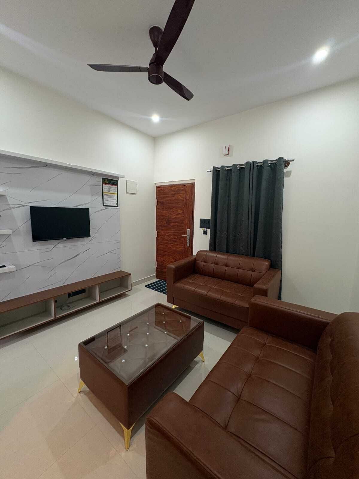 Una sala de estar moderna con televisor de pantalla plana, ventilador de techo, sofá de cuero marrón y una mesa de centro de vidrio.
