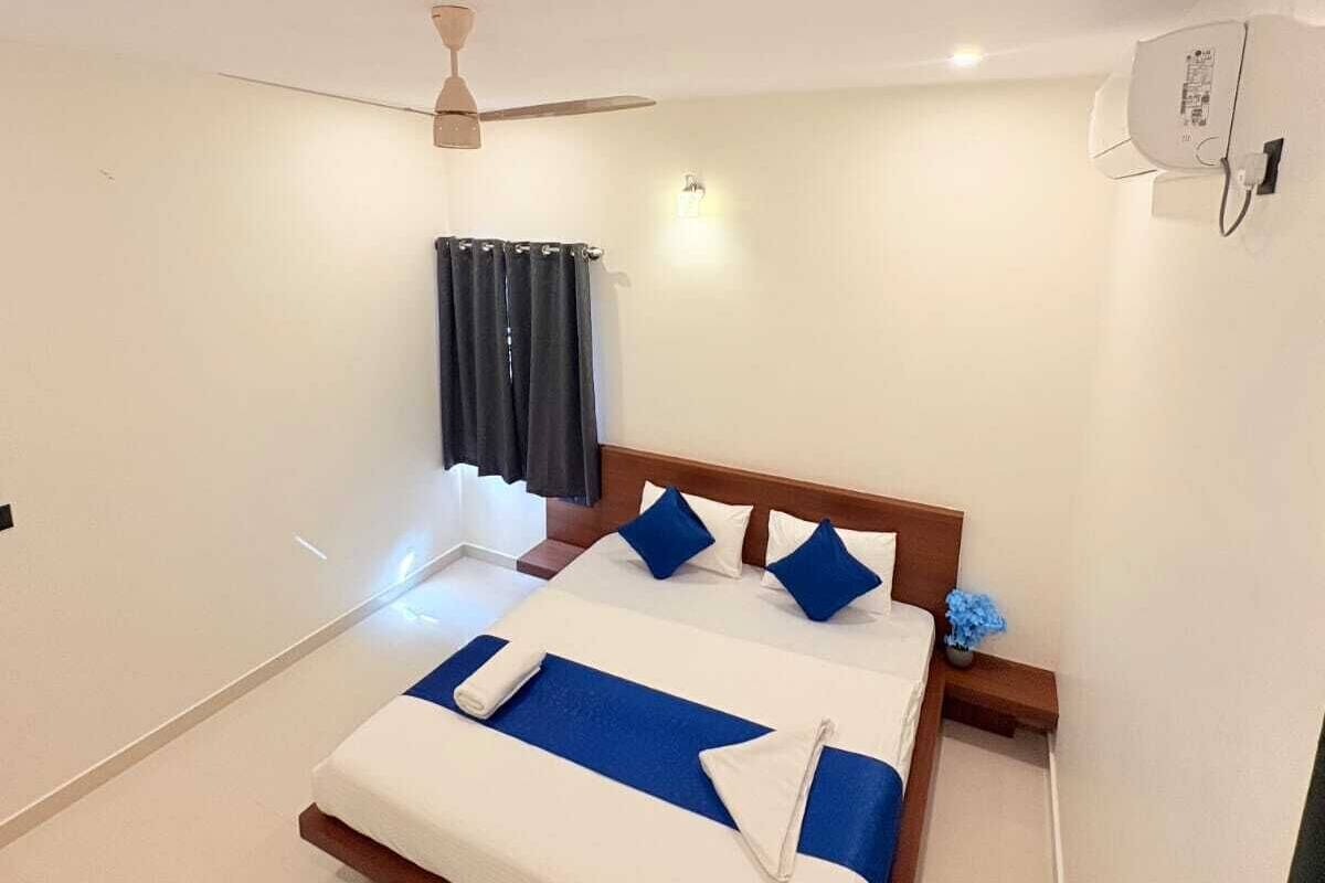 A hotel room with a bed, a ceiling fan, a window with curtains, and a wall-mounted air conditioning unit.