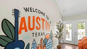 Et værelse med et vægmaleri, der byder besøgende velkommen til Austin, Texas, med et guitarmotiv, bybillede og kaktusser.