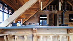 A rustic kitchen with wooden beams, a bar area with stools, and a large window. - CHALET LE CAIRN view of the village Large open spaces 5 minutes from the cable car (Valloire)