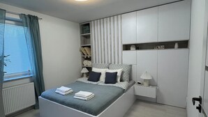 Ein modernes Schlafzimmer mit einem großen Bett, integrierten Stauraumlösungen, einem Heizkörper und einem Fenster mit Vorhängen.