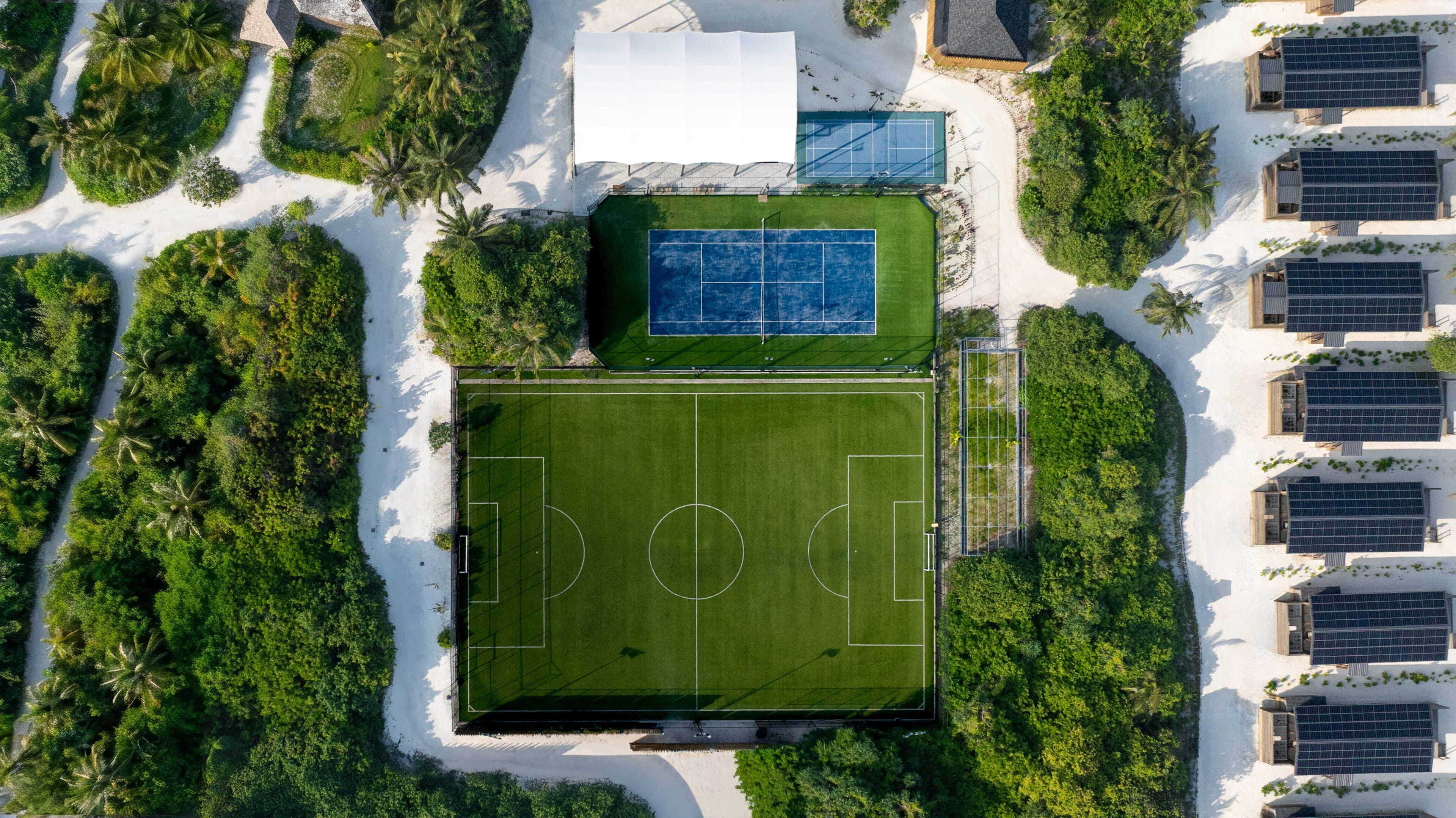 Vista aérea de un complejo deportivo con cancha de fútbol, canchas de tenis y paneles solares.