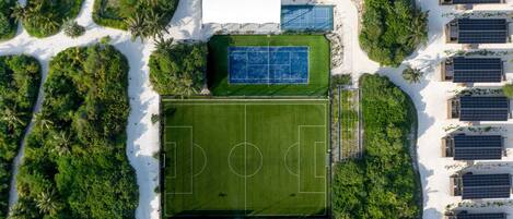 Vista aérea de un complejo deportivo con cancha de fútbol, canchas de tenis y paneles solares.