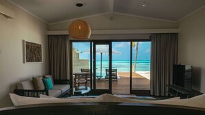 Habitación de hotel con una cama grande, televisión, sofá y vista a la playa y al océano a través de una puerta corrediza.