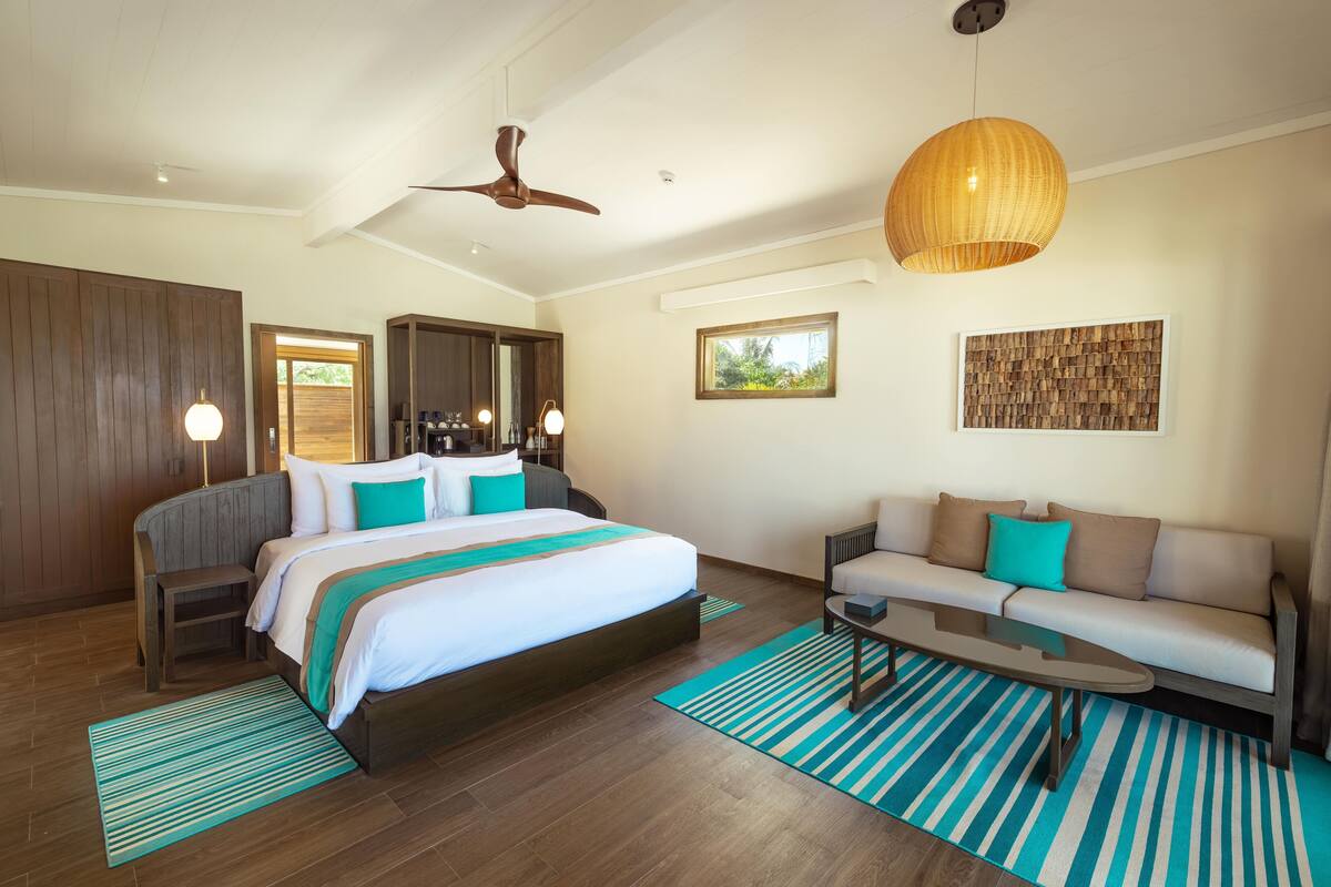Een moderne hotelkamer met een groot bed, een bank, een bijzettafeltje, een plafondventilator en een groot raam.