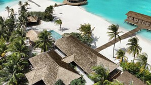 Un resort tropical con bungalows sobre el agua, una playa y aguas turquesas cristalinas.