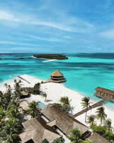 Un resort tropical con bungalows sobre el agua, una playa y aguas turquesas cristalinas.