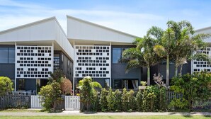 Um edifício moderno com telhado plano, grandes janelas e um jardim bem cuidado com diversas plantas e uma cerca.
