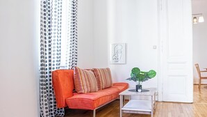 A living room with a red sofa, patterned curtains, a framed artwork, a potted plant, and a wooden floor. - Affordable Apartment Near Stadthalle (Vienna)