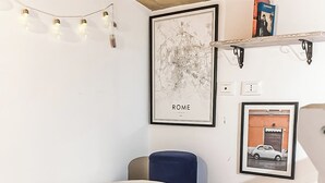 Quarto com cama, um espaço de estar pequeno, um mapa de Roma e uma estante com livros.