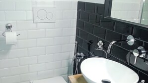 Uma casa de banho moderna com sanita branca, lavatório branco e parede revestida a mosaicos negros.