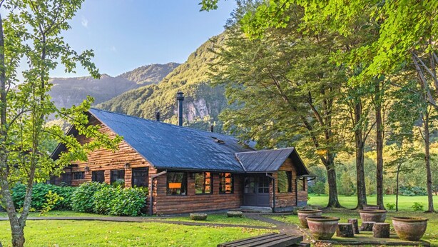 Un chalet rustique en rondins de bois, doté d’un toit en pente, entouré d’une pelouse bien entretenue et de grands jardinières.