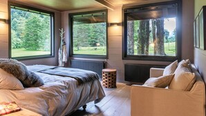 Une chambre à coucher avec un lit, un canapé et de grandes fenêtres donnant sur la forêt.