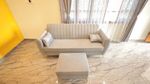 Una sala de estar moderna con un sofá y un reposapiés grises, suelo de mármol y una pared de acento amarilla.