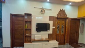 Una sala de estar moderna con un televisor de pantalla plana montado en un mueble blanco, puertas de madera y piso de mármol.