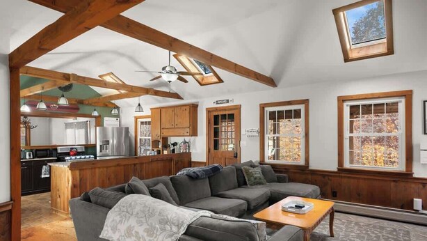 A spacious living area with a sectional sofa, wooden beams, and large windows. - Snow Haus | Hot Tub & Bar | 10 Min to Mount Snow! (Wardsboro)