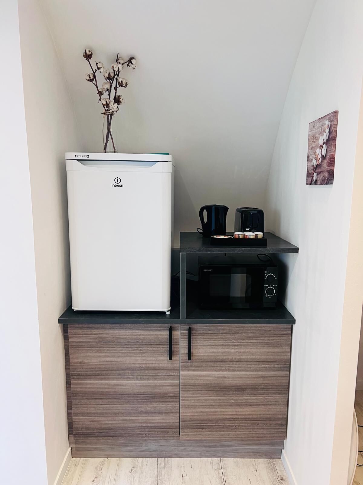 Una kitchenette compacta con un refrigerador blanco, un microondas y una cafetera sobre una encimera negra.