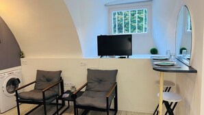 A compact room with a washing machine, two chairs, a TV, and a small table with a mirror. - Relax Studio (Jougne)