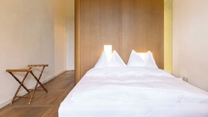 A neatly made bed with white linens, a wooden headboard, and a small wooden folding chair. - Hotel St. Petersinsel (Twann)