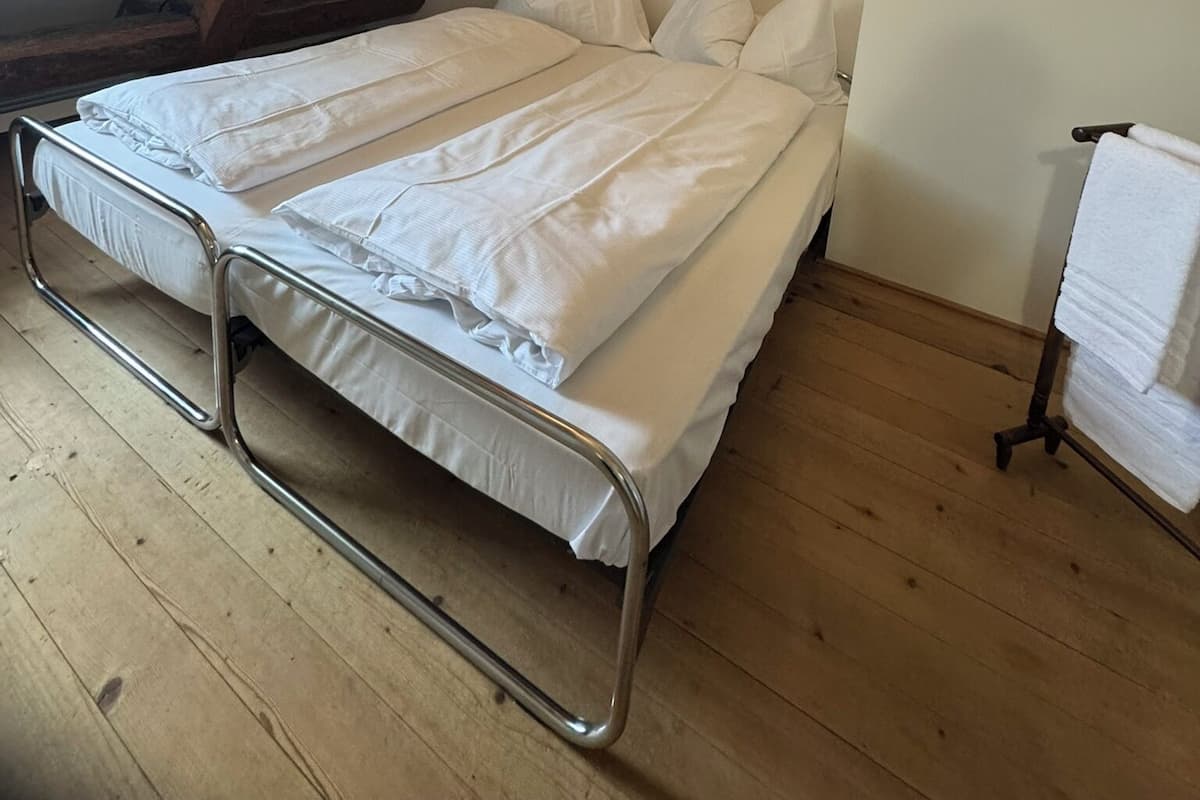 Yhden hengen sänky huoneessa, jossa on puupalkit ja kalteva katto.