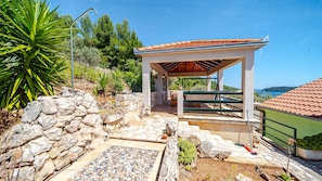 Ein überdachter Außenbereich mit Steinmauern, einer Pergola und Blick auf das Meer.