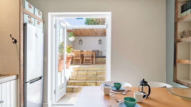 A kitchen with a wooden table set for dining, a refrigerator, and a view of an outdoor patio with a table and chairs. - Delightful cottage in the middle of De Waterkant with all the comforts. (Cape Town)