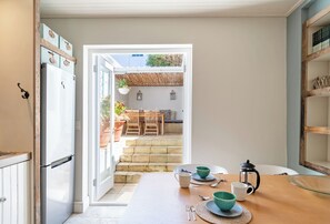 A kitchen with a wooden table set for dining, a refrigerator, and a view of an outdoor patio with a table and chairs. - Delightful cottage in the middle of De Waterkant with all the comforts. (Cape Town)