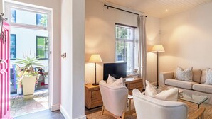 A modern living room with a sofa, chairs, a TV, and a desk with a lamp. - Delightful cottage in the middle of De Waterkant with all the comforts. (Cape Town)