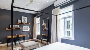 A bedroom with a bed, a desk, a chair, a mirror, and a window with curtains. - Delightful cottage in the middle of De Waterkant with all the comforts. (Cape Town)