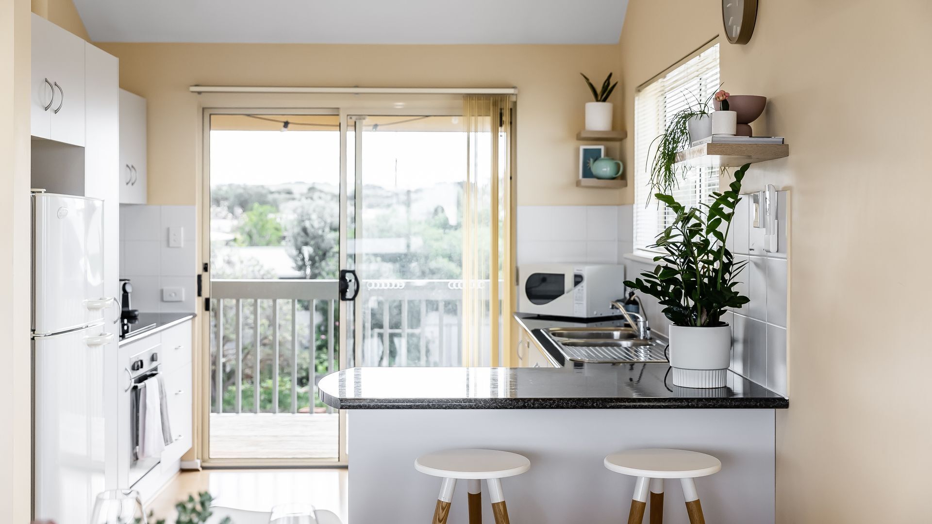 Una cocina moderna con encimera negra, armarios blancos y una puerta corrediza de vidrio que da a un balcón.