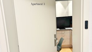 Eine Tür mit der Aufschrift "Apartment 3", die in eine moderne Küche mit Holzboden, einem Stuhl und Schränken führt.