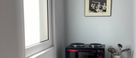 A kitchen with a microwave oven, a framed picture on the wall, and a shelf with kitchen utensils.