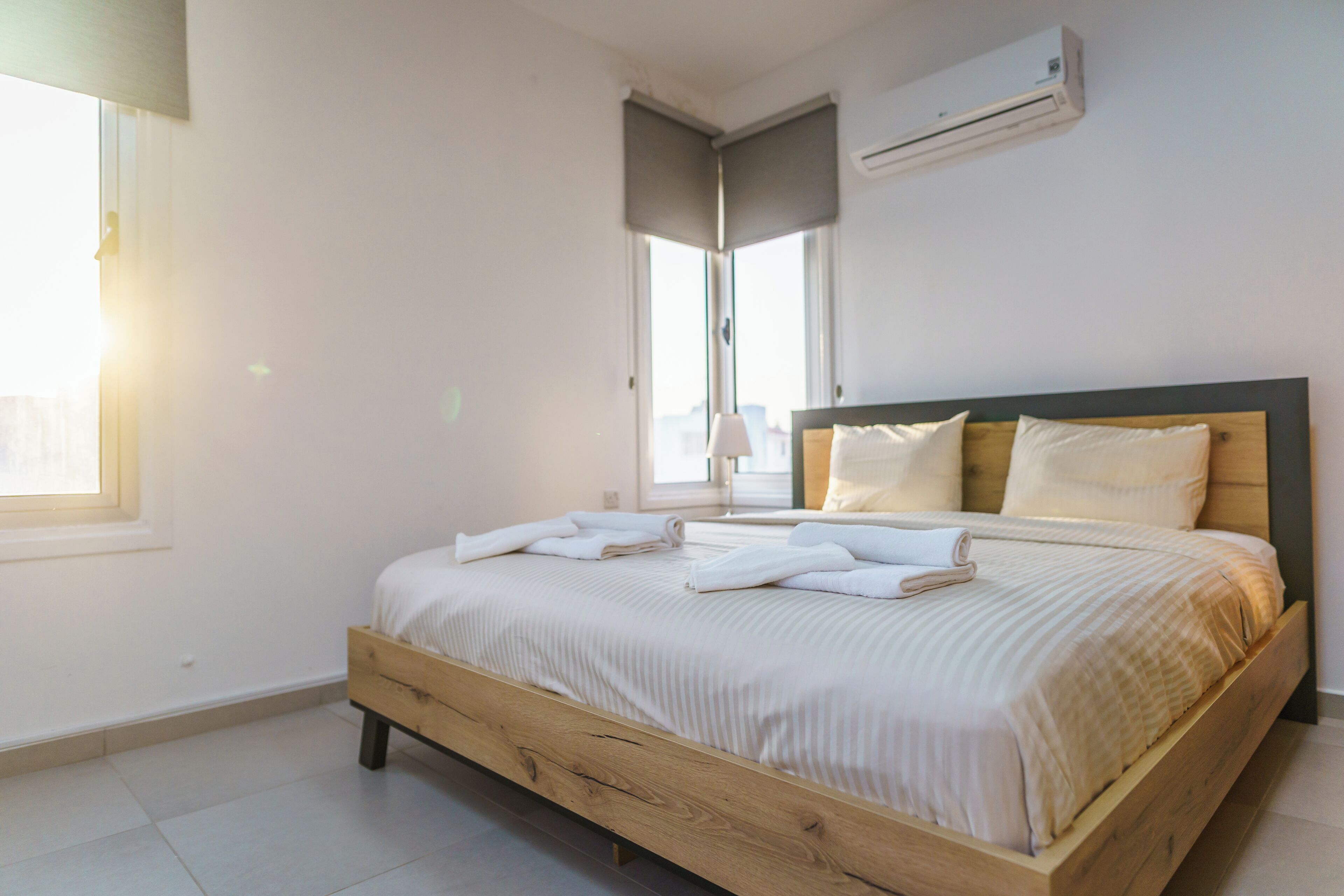 A neatly made bed with white linens and towels, a wooden headboard, and an air conditioning unit on the wall.