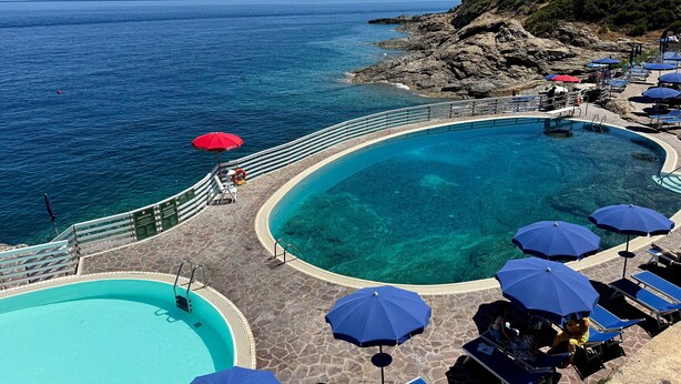 Ein Poolbereich mit klarem, blauem Wasser, ein separater kleinerer Pool und Liegestühle mit Sonnenschirmen.