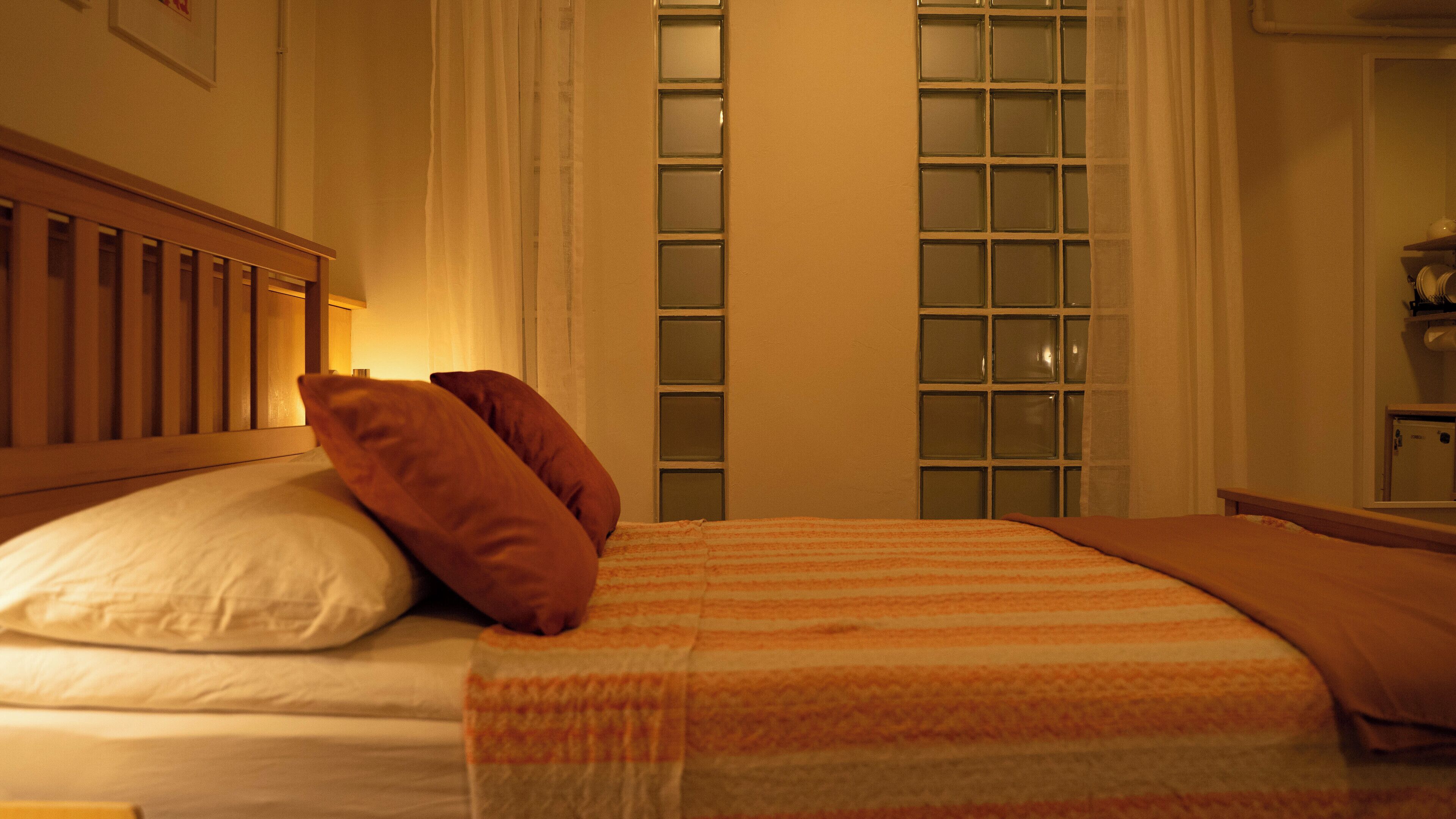 A hotel room with a bed, pillows, a window with curtains, and a wooden headboard.