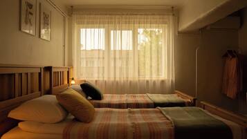 Habitación con dos camas, una ventana con cortinas ligeras y un calentador en la pared.