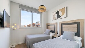 Ein Schlafzimmer mit zwei Betten, einem Fenster, einer Hängelampe und einem Wandbild.