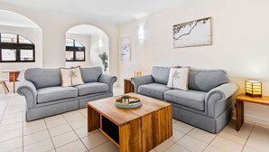 Un salon moderne avec deux canapés gris, une table basse en bois et une petite table d’appoint avec une lampe.