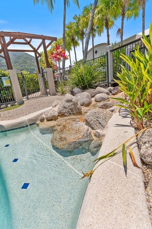 A pool area with clear water, surrounded by rocks and plants, and a pergola structure. - Salt Sand Retreat 1BR Resort Spa (Cairns)