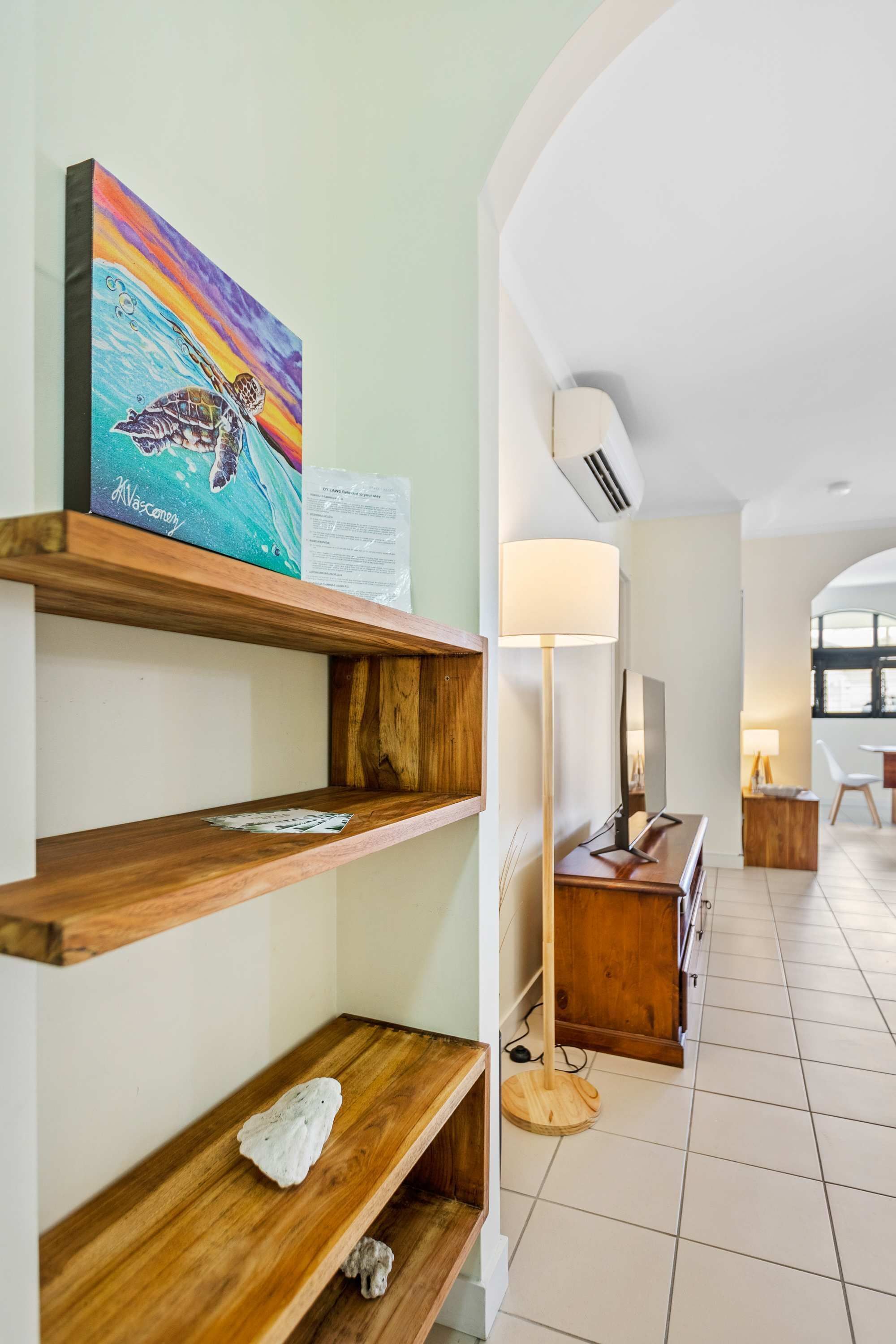 A modern interior with wooden shelves, a painting, a lamp, and a view into a dining area.