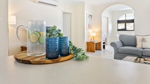 Un salon moderne avec un pichet en verre et des verres bleus posés sur un plateau en bois, un canapé gris et une petite table avec une lampe.