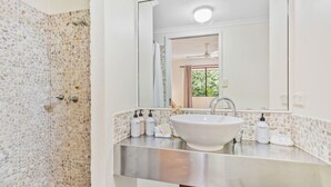 A bathroom with a stone shower wall, a white sink, and a mirror above it. - Palm Cove Studio Pools Spa Bar (Cairns)
