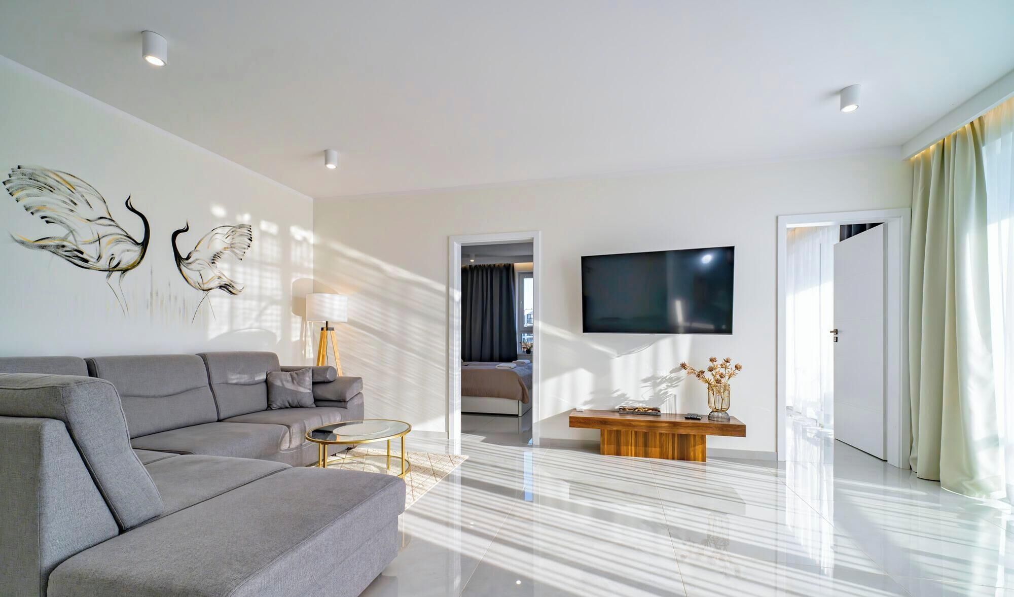 A modern living room with a grey sofa, a coffee table, and a flat-screen TV mounted on the wall.