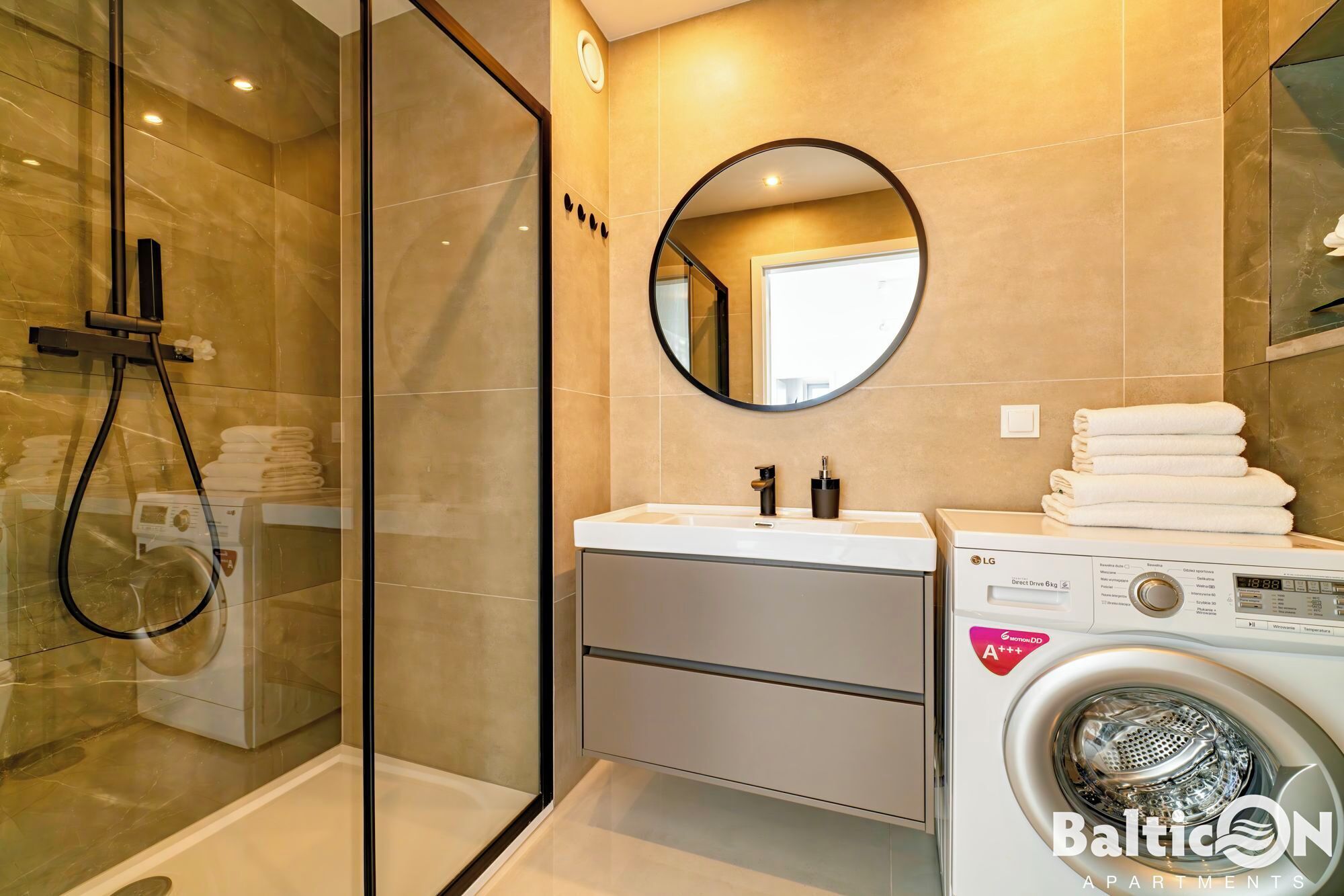 A modern bathroom with a glass-enclosed shower, a sink with a mirror, and a front-loading washing machine.